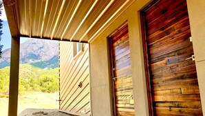 A covered porch with wooden slats, a concrete bench, and two wooden doors. - Architectural Peace and Perfection in the Sandia Mountains (Albuquerque)