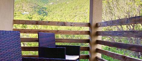 Un balcon doté de meubles en osier et offrant une vue sur un paysage montagneux.