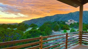 A balcony with a wooden railing overlooking a mountainous landscape with a white building. - Architectural Peace and Perfection in the Sandia Mountains (Albuquerque)