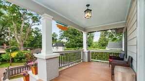 Une véranda couverte avec un plancher en bois, des balustrades blanches et une lanterne suspendue.