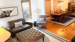Ein Wohnzimmer mit einer Couch, einem Hocker und einem Essbereich mit Tisch und Stühlen.