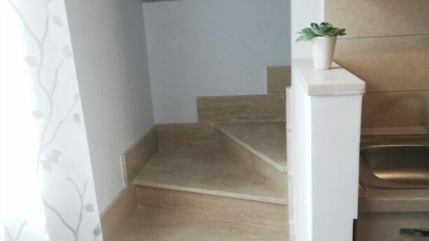 Un escalier menant à l’étage supérieur, une petite plante en pot sur le palier et un coin cuisine avec des placards.