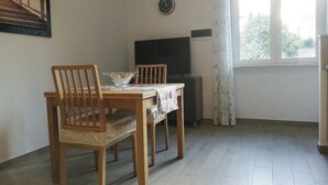 Un coin repas avec une table et des chaises en bois, un téléviseur et une fenêtre avec des rideaux.