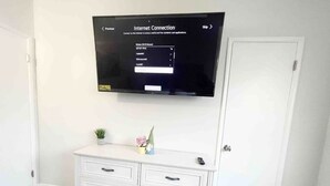 A room with a white dresser, a flat-screen TV mounted on the wall displaying an 'Internet Connection' screen, and a small plant on the dresser.