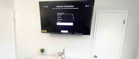 A room with a white dresser, a flat-screen TV mounted on the wall displaying an 'Internet Connection' screen, and a small plant on the dresser.