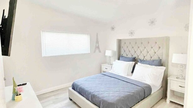 A bedroom with a bed, bedside tables, a dresser, a window with blinds, and a wall-mounted Eiffel Tower decoration.