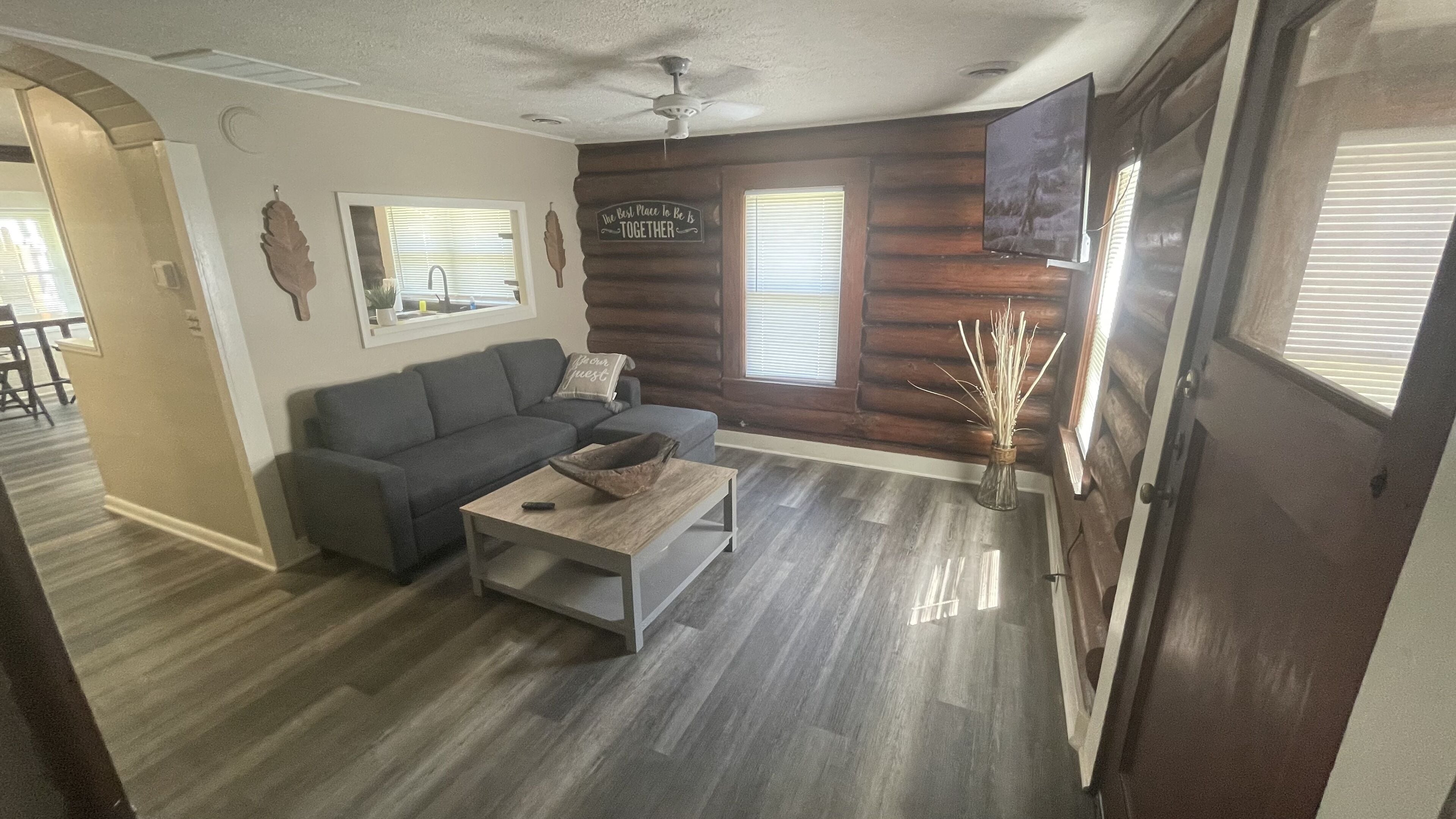A cozy living room with a gray sofa, a coffee table, and a TV mounted on the wall.