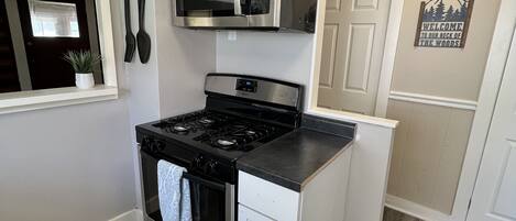 Uma cozinha com armários brancos, fogão de aço inoxidável e micro-ondas. Há uma placa na parede com a inscrição 'Bem-vindos ao nosso cantinho.'