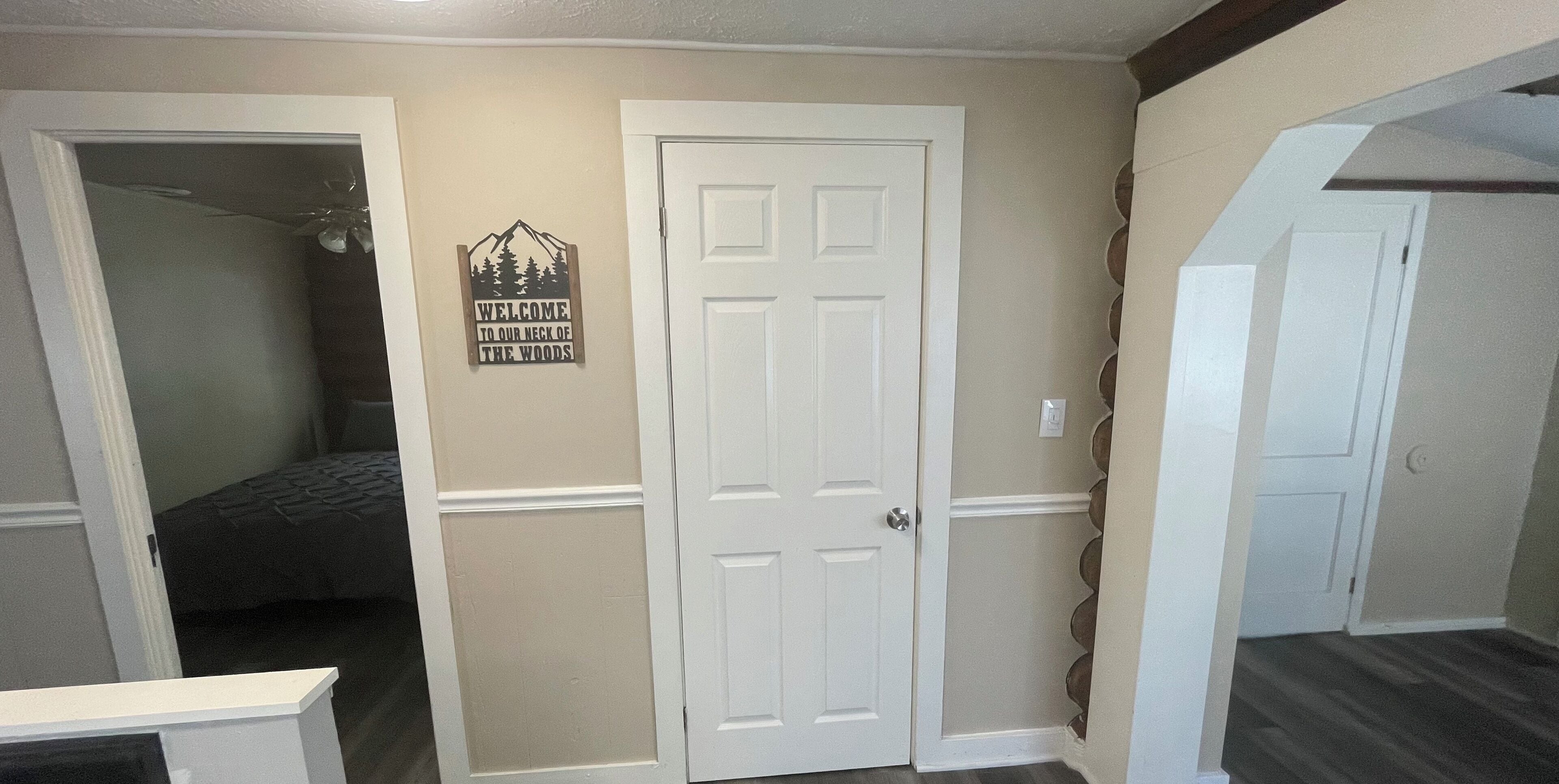 A hallway with a door, a bed, and a welcome sign.