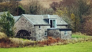 A stone building with a large wheelhouse, surrounded by a grassy field and trees. - Restored watermill with stunning views of Loch Fyne (Kilfinan)