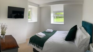 A bedroom with a bed, a TV mounted on the wall, and two windows. - Restored watermill with stunning views of Loch Fyne (Kilfinan)