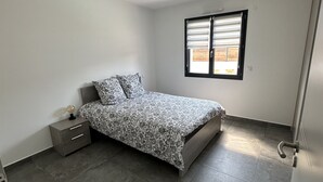 Ein Schlafzimmer mit einem Bett, einem Nachttisch, einem Fenster mit Jalousien und einer Tür.