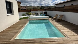 Ein rechteckiger Pool mit Holzterrasse, umgeben von weißen Wänden und einem Holzzaun.