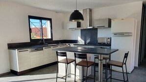 Eine moderne Küche mit einer zentralen Kochinsel, Barhocker, einem Einbauofen und einem Fenster mit Ausblick.