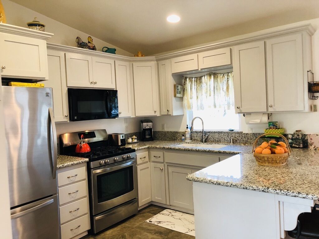 A kitchen with white cabinets, stainless steel appliances, a granite countertop, and a window with curtains.