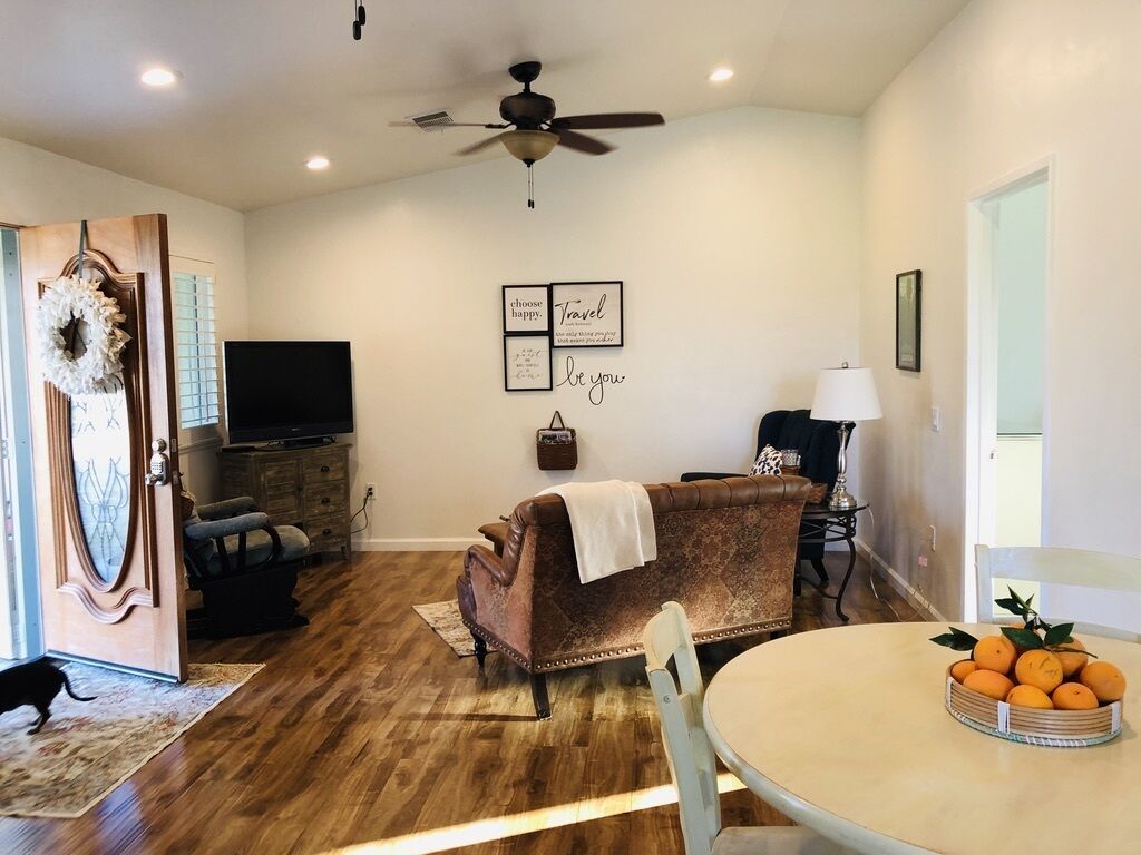 A living room with a brown leather sofa, a television, a ceiling fan, and a table with oranges.