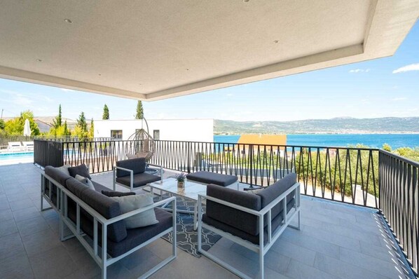 A covered outdoor seating area with a pool view, a white building, and a clear blue sky.