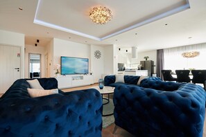 A modern living room with a large sectional sofa, a flat-screen TV, and a dining area with a kitchen in the background.
