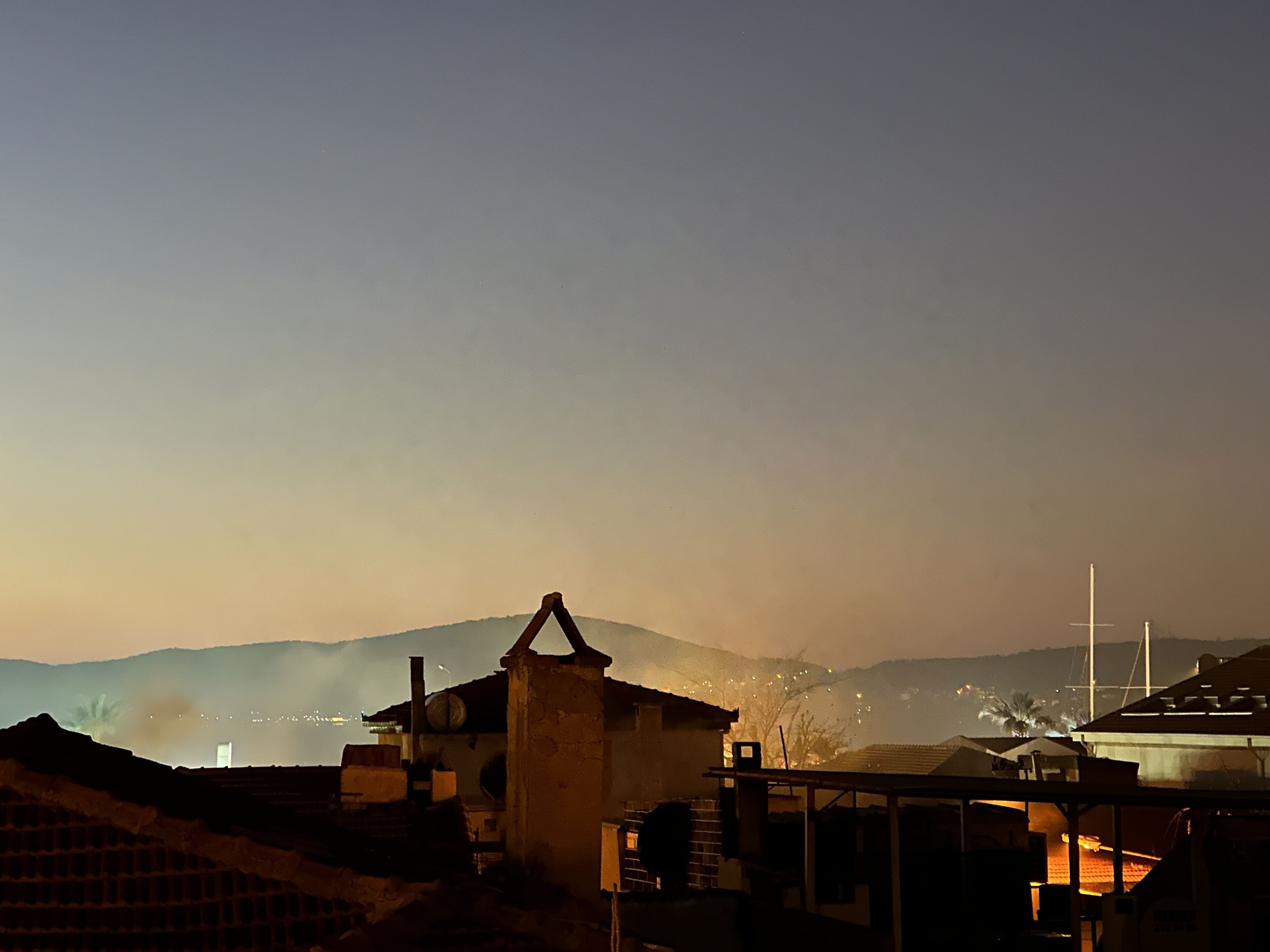 A coastal village at dusk with traditional buildings, a prominent church steeple, and distant mountains.