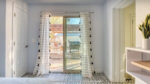 Ein Zimmer mit einer Schiebetür, einem gemusterten Boden und Blick auf einen Außenbereich mit einer Holzkonstruktion und einem Stuhl.