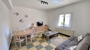 Ein Wohnzimmer mit Schachbrettmuster-Boden, einer Couch, einem Fernseher und einem Essbereich mit Stühlen und einem Tisch.