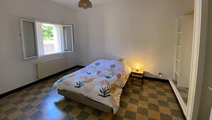 Ein Schlafzimmer mit einem Bett, einem Fenster, einem Heizkörper und einem kleinen Nachttisch mit einer Lampe.