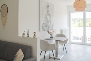 A modern living room with a gray sofa, a dining table with chairs, a large wall painting, and a hanging light fixture.