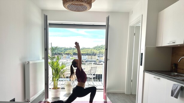 Un tapis de yoga est posé sur le sol, et on peut voir, à travers une porte, un paysage urbain.