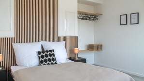 Une chambre à coucher bien rangée, avec un lit, des oreillers, une lampe de chevet et une étagère fixée au mur.