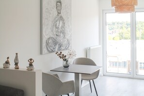Un comedor moderno con una mesa minimalista, dos sillas, un jarrón con flores y un cuadro grande de Buda en la pared.