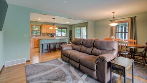 A spacious living room with a brown leather sofa, a dining area with a wooden table and chairs, and a kitchen with wooden cabinets and a central island.