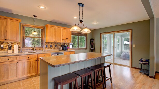 A kitchen with wooden cabinets, a large island with stools, and a view to the outside.