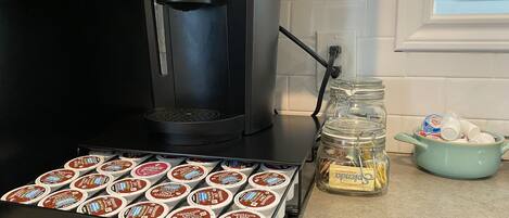A coffee maker on a kitchen counter with a drawer of coffee pods and a jar of butter.