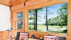 Una cabaña de madera con dos sillas, una mesa, un telescopio y vistas a un bosque y un lago.