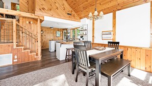 A wooden interior with a dining area, kitchen, and staircase.