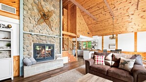A spacious living room with a stone fireplace, wooden beams, and a cozy brown leather sofa.