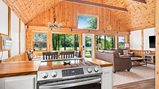 A modern kitchen with a wooden ceiling, large windows, and a dining area.