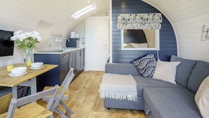 A compact, modern living space with a kitchenette, a dining area with a table and chairs, and a cozy seating area with a sofa and cushions.