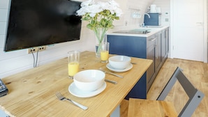 A modern kitchen with a wooden dining table, two white bowls, a glass of orange juice, and a vase with white flowers.