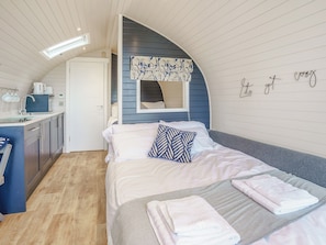 Een kleine slaapkamer met een bed, nachtkastje en een kitchenette.