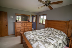A bedroom with a wooden bed, a dresser, a ceiling fan, and two windows.