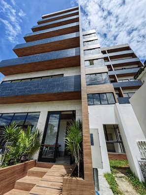 A modern multi-story building with a combination of wooden and stone facade elements, large windows, and a well-maintained outdoor area with planters and steps.