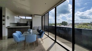 Un appartement moderne doté d’un balcon, d’un coin repas avec des chaises bleues et d’une cuisine avec des meubles blancs.