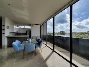 A modern apartment with a balcony, a dining area with blue chairs, and a kitchen with white cabinets.