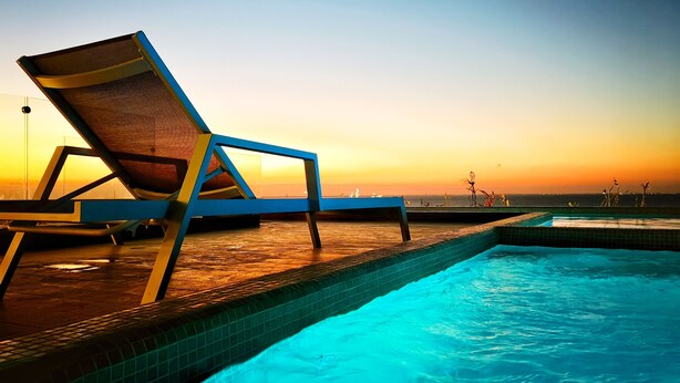 Un espace aménagé au bord de la piscine, avec un fauteuil et une vue sur le coucher de soleil sur l’eau.