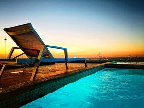 A poolside area with a lounge chair and a view of the sunset over the water. - Stylish 2-bedrooms Condo in the Heart of Cozumel Mexico (Cozumel)