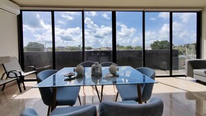 Un espace de salle à manger moderne avec une table en verre et des chaises bleues, de grandes fenêtres offrant une vue sur le paysage urbain.
