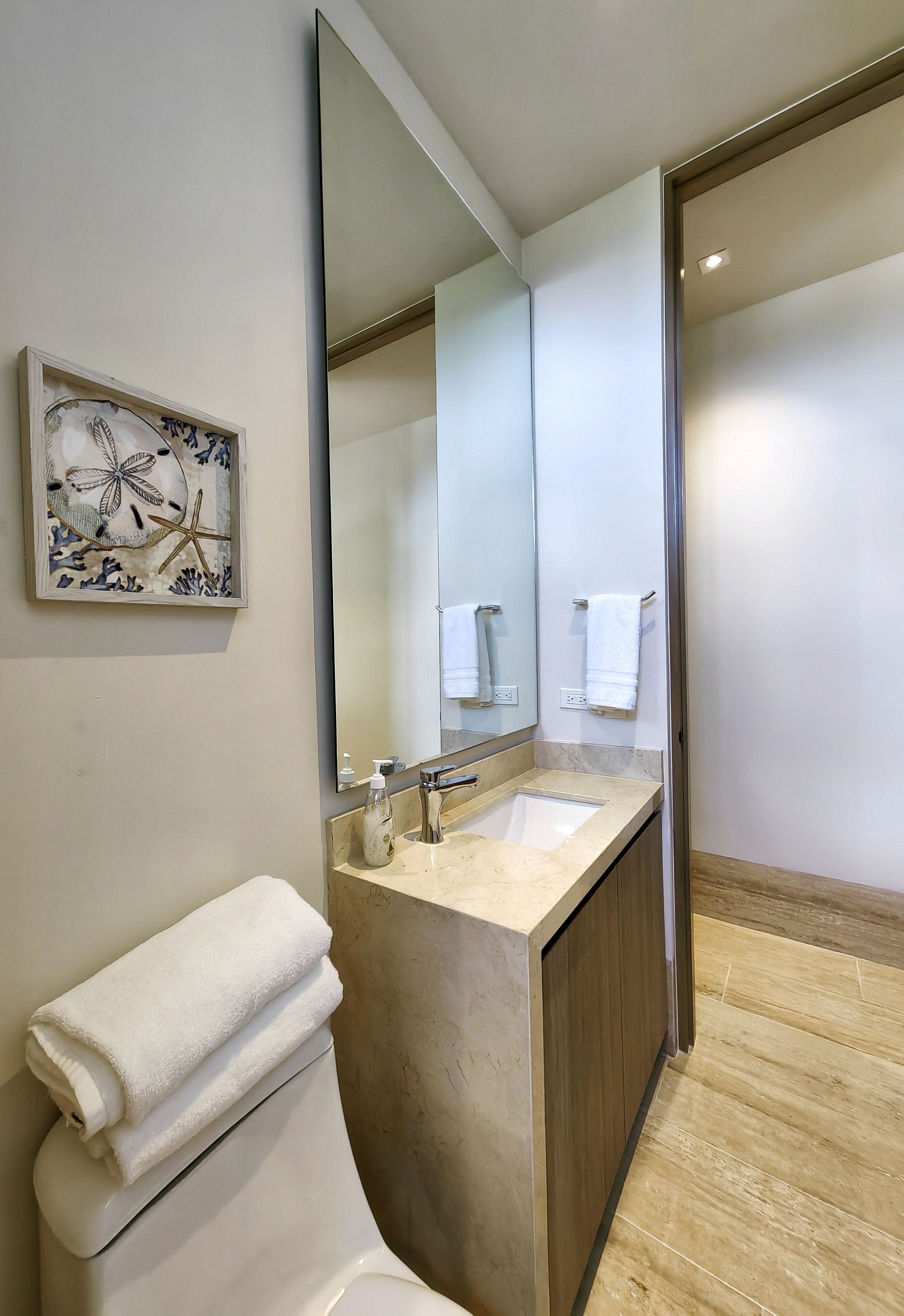 Une salle de bain moderne avec un grand miroir, un lavabo et des toilettes. On y trouve un porte-serviettes sur lequel est accrochée une serviette.