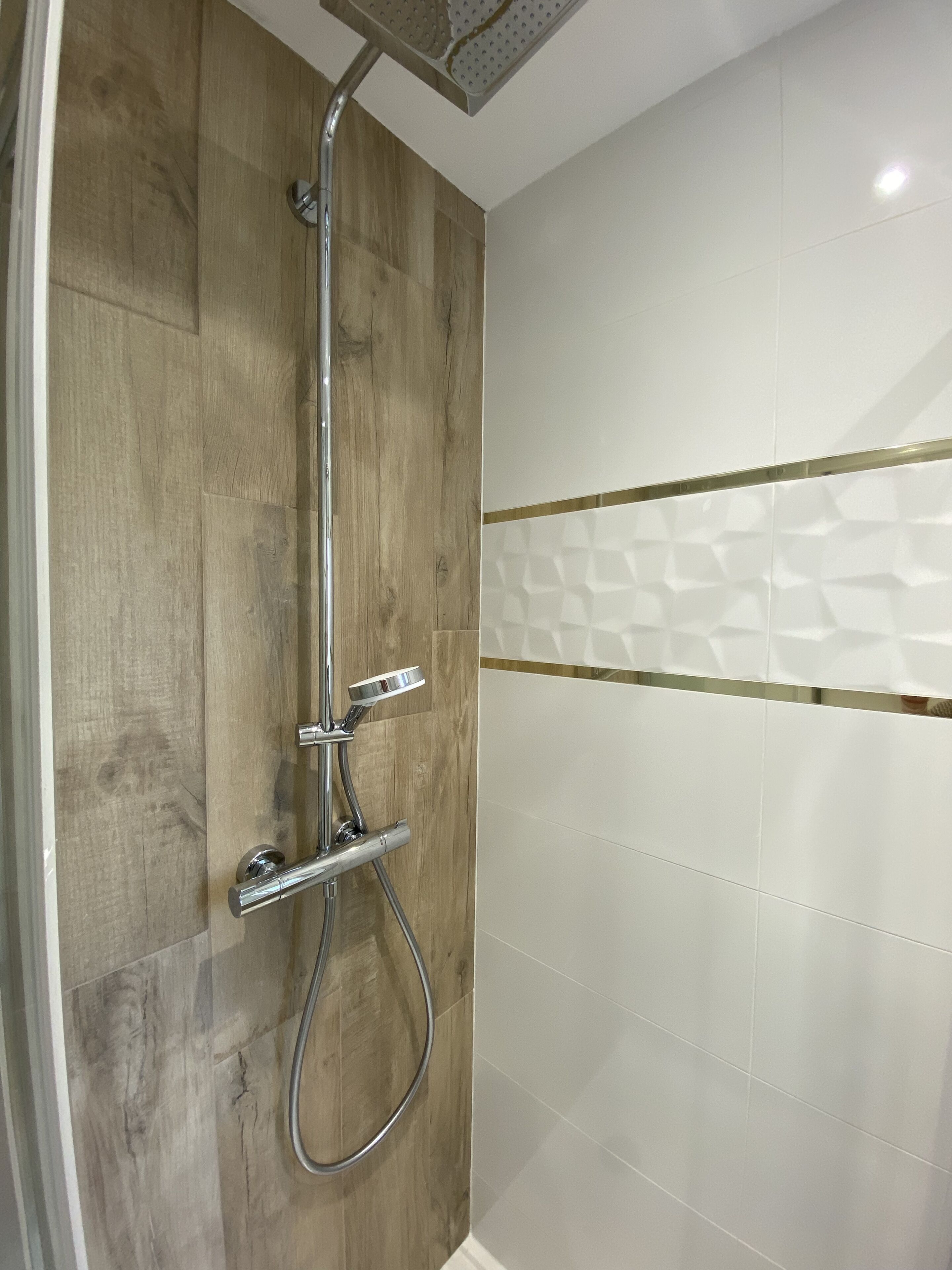Une douche avec un mur en panneaux de bois et une partie recouverte de carreaux blancs.