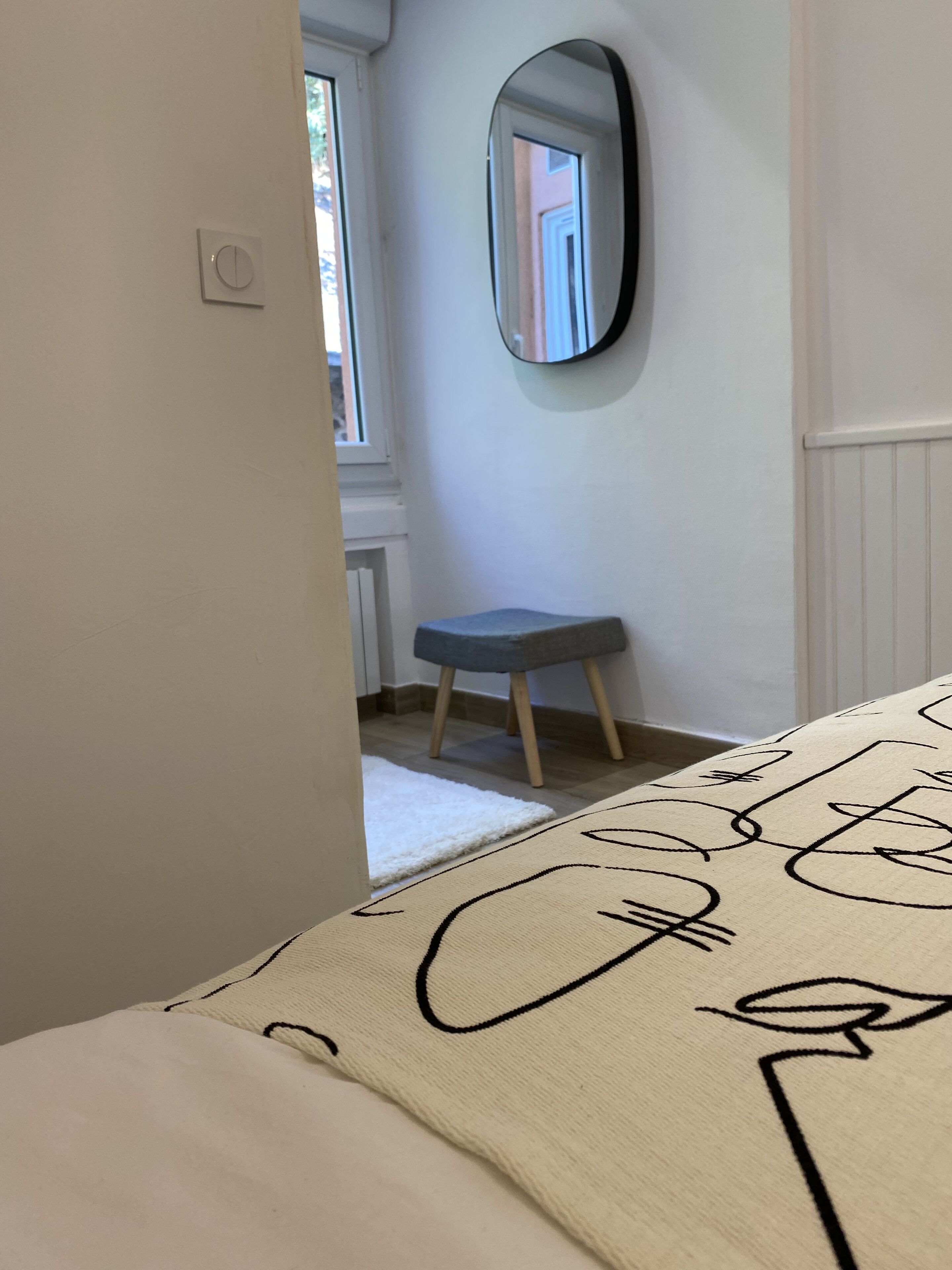 Ein Schlafzimmer mit einem Bett, einem kleinen Hocker, einem Wandspiegel und einer Heizung.